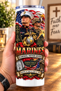 Hand holding a straight-sided 20 oz tumbler with Patriotism Marine 2 artwork on a warm wood counter