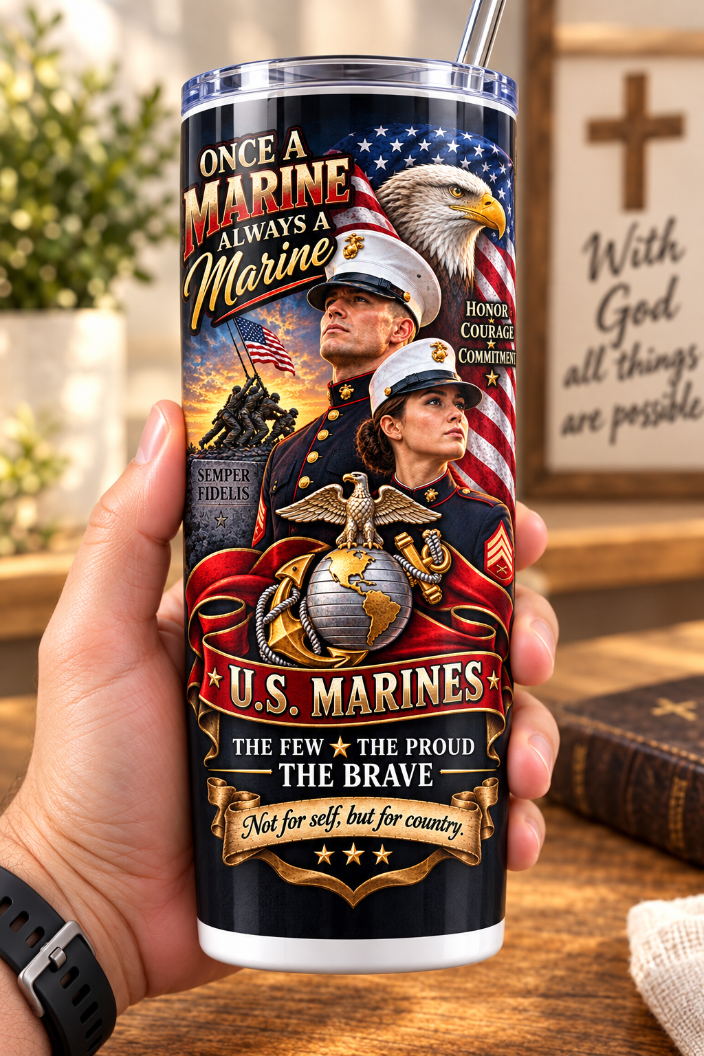 Hand holding a straight-sided 20 oz tumbler with Patriotism Marine 1 artwork on a warm wood counter