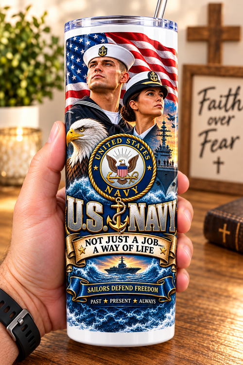Hand holding a straight-sided 20 oz tumbler with Patriotism Navy 1 artwork on a warm wood counter