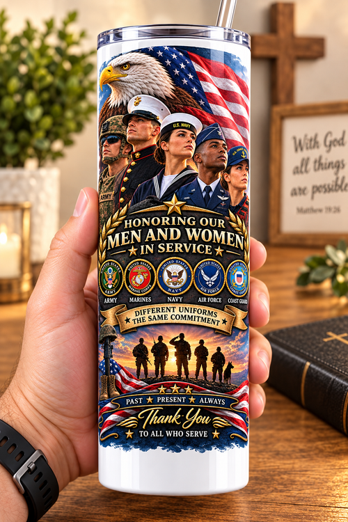 Hand holding a straight-sided 20 oz tumbler with Patriotism Armed Services artwork on a warm wood counter